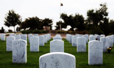 An image of a tombstone in a cemetery. The tombstone has the symbol for atheism on it where a religious symbol would normally be located.