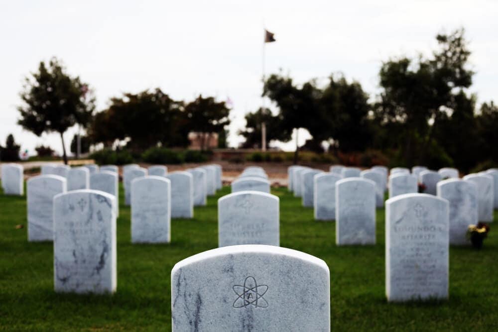 An image of a tombstone in a cemetery. The tombstone has the symbol for atheism on it where a religious symbol would normally be located.